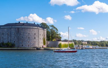 Vaxholm, İsveç - 13 Eylül 2025: Güneşli bir günde tarihi bir taş kalenin yanından bir yelkenli geçiyor.