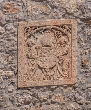 Skofja Loka, Slovenya - 30 Temmuz 2025: Duvarda, karmaşık oymalar ve Latince yazıtlarla bir kalkan tutan iki figürü tasvir eden taş tasviri.