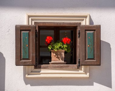 Ahşap kepenkleri ve saksıda kırmızı bir sardunyası olan kırsal bir pencere..