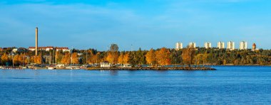 Stockholm, İsveç - 18 Ekim 2025: Sonbahar ağaçları, binalar ve açık gökyüzü olan bir göl manzarası.