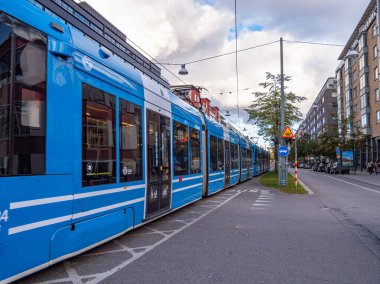 Stockholm, İsveç - 18 Ekim 2025: Ağaçlı ve binalı bir şehir caddesinde mavi tramvay