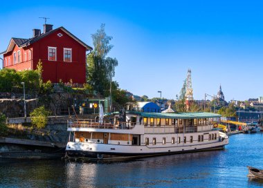 Stockholm, İsveç - 3 Ekim 2025: Güneşli bir günde kırmızı bir eve yanaşmış bir teknenin manzaralı manzarası.