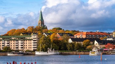 Stockholm, İsveç - 19 Ekim 2025: Kilise, nehir ve sonbahar ağaçlı bir Avrupa şehrinin manzarası.