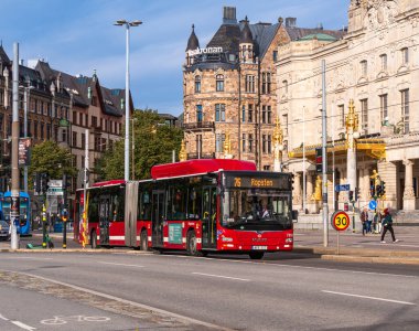 Stockholm, İsveç - 11 Ekim 2025: Arka planda tarihi binalar bulunan bir caddede kırmızı şehir otobüsü.