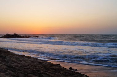 Sıcak bir yaz sabahında dalgalarla deniz kıyısında gün doğumu