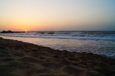 Sıcak bir yaz sabahında dalgalarla deniz kıyısında gün doğumu