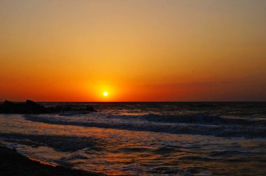 Sıcak bir yaz sabahında dalgalarla deniz kıyısında gün doğumu