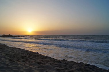 Sıcak bir yaz sabahında dalgalarla deniz kıyısında gün doğumu