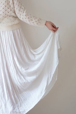 Beyaz etek giyen bir kadının yakın çekimi. Kameraya geri dönelim, beyaz bir arka planda krem rengi yumuşak kazak ve açık renkli elbise giymiş beyaz bir kadın.