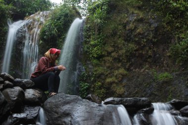 Güzel bir şelalenin önünde duran bir kadın. 