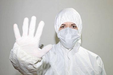 Koronavirüsle savaşmak için koruyucu maskeli ve tulumlu bir kadın sağlık görevlisi durduğunun işareti olarak elini kaldırır. Halk sağlığı kavramı