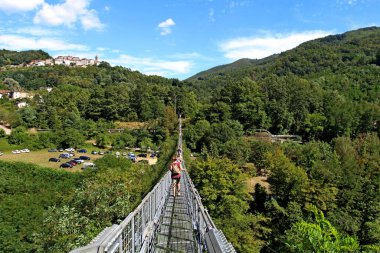 San Marcello Piteglio, Pistoia, Italy - August 23, 2020: the suspension bridge of the Ferriere. Opened in 1923, it measures 227 meters in length, 36 meters in height and 80 centimeters in width. clipart