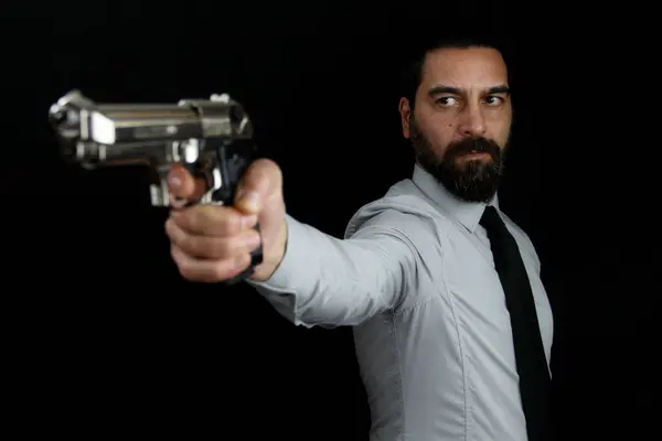 Siyah arka planda sakallı yakışıklı bir adam eline silah tutarak onu önüne doğrultuyor. Gangster, polis.