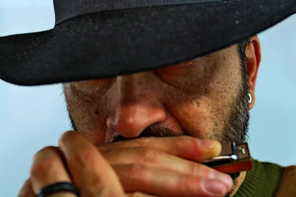 Close-up, a cowboy plays the harmonica in his mouth with his hat covering his eyes. Western spaghetti