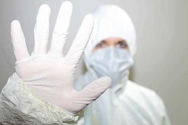 a female health worker with coverall and protective mask to fight coronavirus raises her hand as a sign of stopping. Public health concept