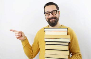 İzole edilmiş beyaz arka planda gözlüklü sakallı adam elinde bir yığın kitap tutarken parmağıyla kenarı işaret ediyor.