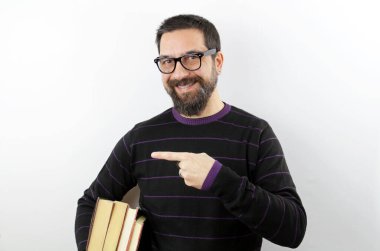 Gözlüklü sakallı adam kitaplarını kolunun altında tutuyor. Beyaz arka planda gülümsüyor, el ve parmaklarıyla işaret ediyor.