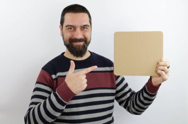 Sıradan kıyafetler giyen, elinde parmağıyla işaret eden boş bir pankart tutan gülümseyen sakallı adam.