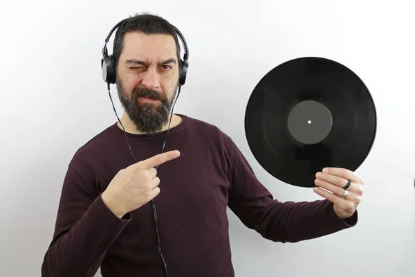 Sakallı adam müzik dinliyor. Kulaklık kullanıyor. Elinde vinil disk var.