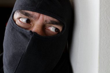 Evin içinde birini beklerken kar maskeli bir soyguncu duvarın arkasında saklanıyor. Soygun konsepti