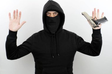 Yüz maskesi takan, elinde kelepçe ve tabanca tutan siyah kapüşonlu beyaz arka plandaki kameraya bakan bir suçlu. Suç kavramı