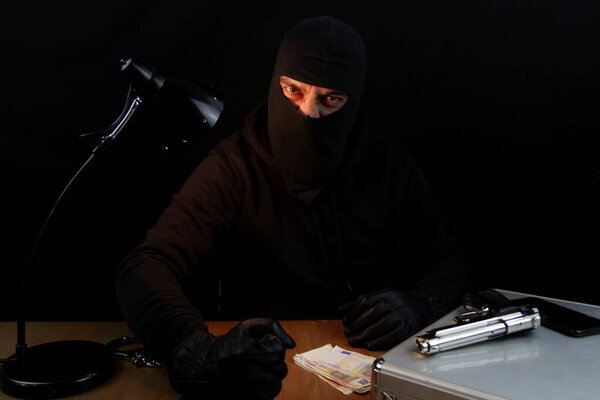 Man wearing balaclava with angry expression and furious banging fists on the table, on black background.