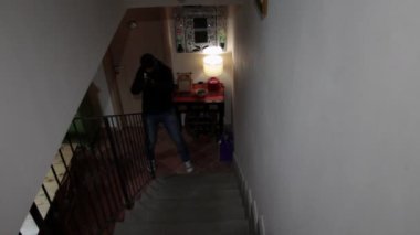 Yüzü kapalı tehlikeli bir tetikçi, bir evin içinde kurbanı aramak için merdivenlerden çıkar.