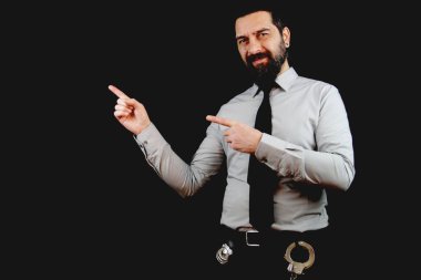 Sakallı dedektif kameraya bakarken gülümsüyor. İki eli ve parmağı yana bakıyor. Siyah arkaplanda izole. 