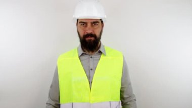 Güvenlik gözlüğü ve iş kaskı takan inşaat mühendisi izole edilmiş beyaz arka planda duruyor. Yavaş çekim.