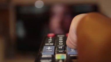 Kanal değiştirirken uzaktan kumandayı elinde tutan bir adam.