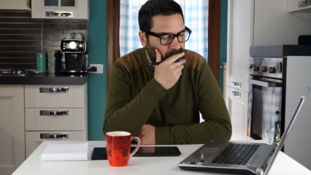 一个留着胡子的男人在电脑上工作 他从家里思考问题 把目光移开 考虑风险 找到解决问题的办法 在笔记本上写笔记 聪明的工作概念 — 图库视频影像