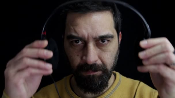 Großaufnahme Setzt Sich Ein Bärtiger Mann Auf Schwarzem Hintergrund Kopfhörer — Stockvideo
