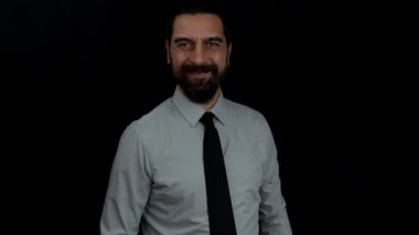 İzole edilmiş siyah arka planda gülümseyen sakallı işadamı kolunu kaldırır ve baş parmağını eliyle öne uzatır. İş konsepti