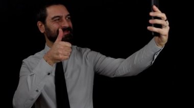 İzole edilmiş siyah arkaplanda gülümseyen sakallı iş adamı cep telefonundan bir video çağrısında. İş konsepti