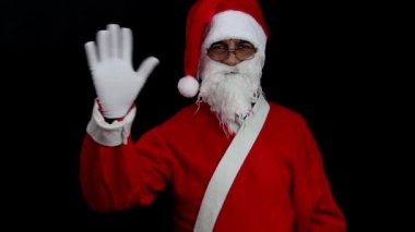 Siyah arka planda gülümseyen Noel Baba kolunu kaldırıp eliyle selam veriyor. Noel konsepti