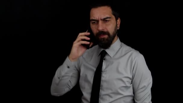 電話で興奮して話して隔離された黒の背景に深刻な顔を持つハンサムなビジネスマン 事業概念 — ストック動画