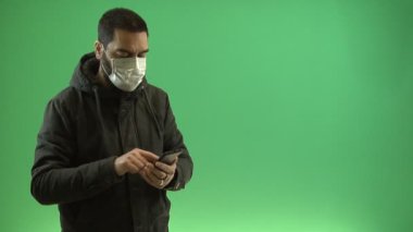 Yeşil arka planda akıllı telefondan koruyucu maskeli bir adam. Krom anahtar