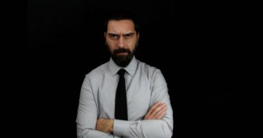 Ciddi yüzlü, gömlekli ve kravatlı sakallı bir adam ve izole edilmiş siyah arka planda çapraz kollar. Yüzünde kafatası röntgeni beliren bir felç etkisi. 4K