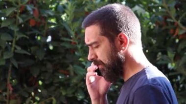 Sakallı bir adam telefonda çitin arkasında ciddi bir yüzle konuşuyor.