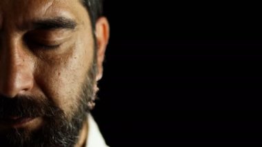Yoğunlaşmış sakallı adamın yarım portresi gözlerini açar ve siyah arka plandaki kameraya bakar..