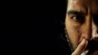 Sigara içen konsantre bir adamın yarım portresi ve siyah arka planda kameraya bakıyor..