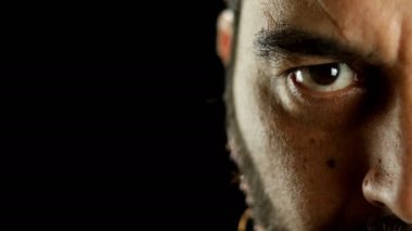 Yoğunlaşmış ve ciddi sakallı bir adamın yarım portresi siyah arka planda kameraya bakıyor..