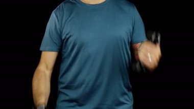 Spor kıyafetli bir adam 3 kiloluk halterlerle biseps yapıyor, siyah arka planda çalışıyor. Sağlığı korumak için spor yapmak. Yüzü yok.