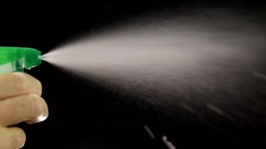 Adamın eli, siyah arka planda damlacıklarla dolu sprey temizleyici şişesini tutuyor. Yavaş çekimde, kapat..