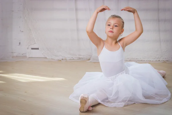 Молодая балерина в белой одежде сидит на полу во время тренировки в танцевальном классе . — стоковое фото