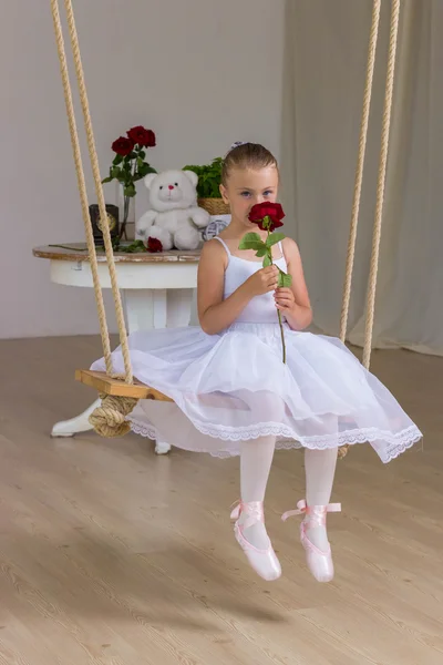 Portrait of little cute ballerina on swing with rose. Princess concept. Fairy tail