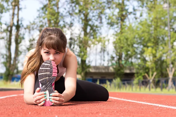 Piękna młoda kobieta w biustonosz sportowy rozciąganie ścięgna udowego na torze — Zdjęcie stockowe