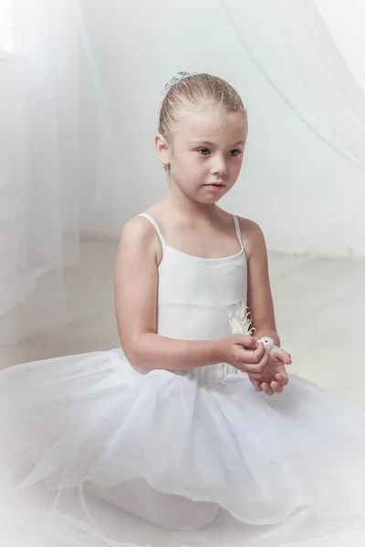 Веселая милая девочка сидит на полу с птицей в руках, маленькая балерина — стоковое фото
