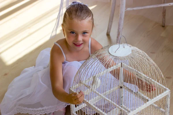 Cheerful cute girl sitting in the floor with bird in cage, little ballerina — Stock Photo, Image