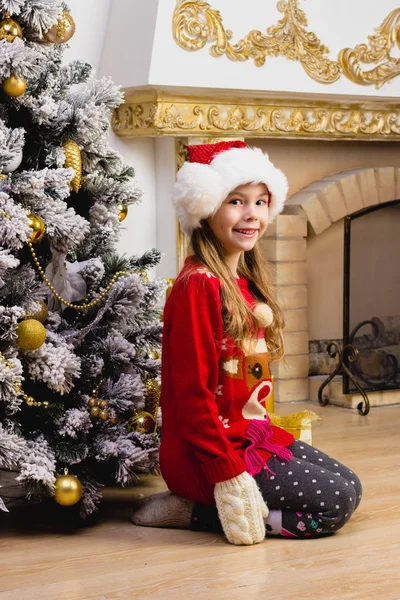 Small cute girl sitting and smilling near the christmas tree — Stock Photo, Image